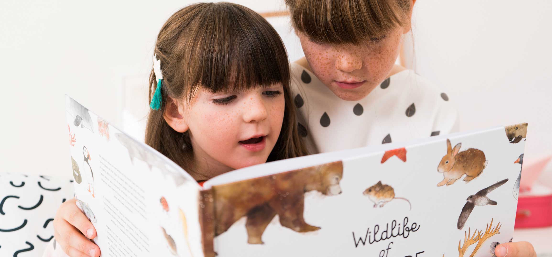 Two girls reading a JUNIQE children's book with animal illustrations